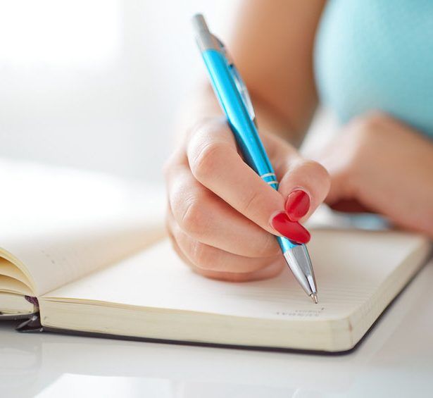 AYoung woman writes to black diary on a white table