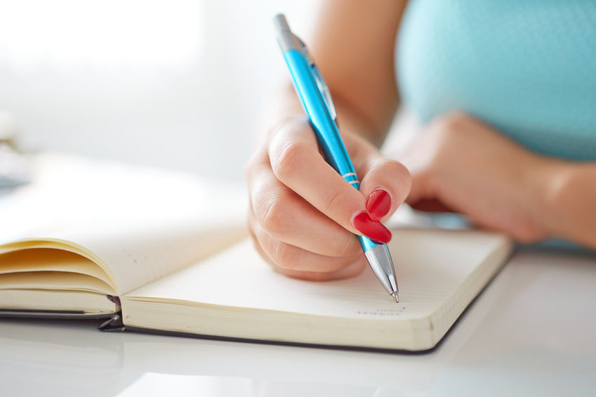 AYoung woman writes to black diary on a white table